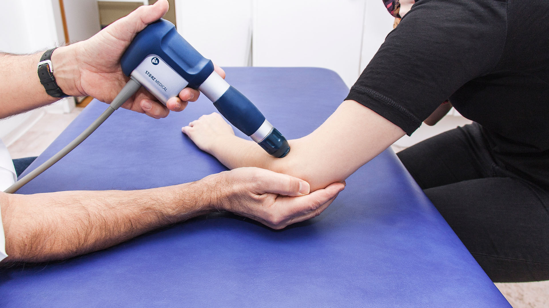 Ein Arzt führt eine Stoßwellentherapie bei seiner Patientin durch.